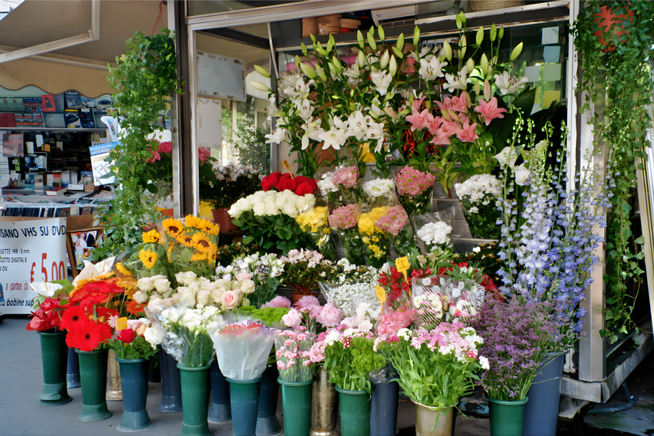 A vibrant display of fresh floral arrangements outside a flower shop, featuring a variety of flowers including white lilies, pink lilies, red gerbera daisies, white roses, pink chrysanthemums, and pur