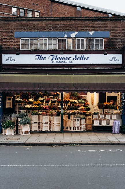 The storefront of The Flower Seller of Muswell Hill showcasing a vibrant display of fresh floral arrangements and bouquets in various colors, including yellows, reds, greens, and purples, arranged on 